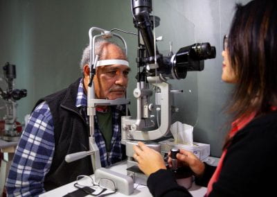 A male eye health survey participant is examined at a slit lamp by a female optometrist