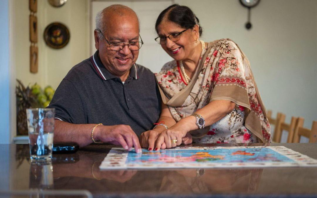 A smiling older couple sit at a table doing a jigsaw together