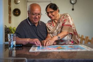 A smiling older couple sit at a table doing a jigsaw together